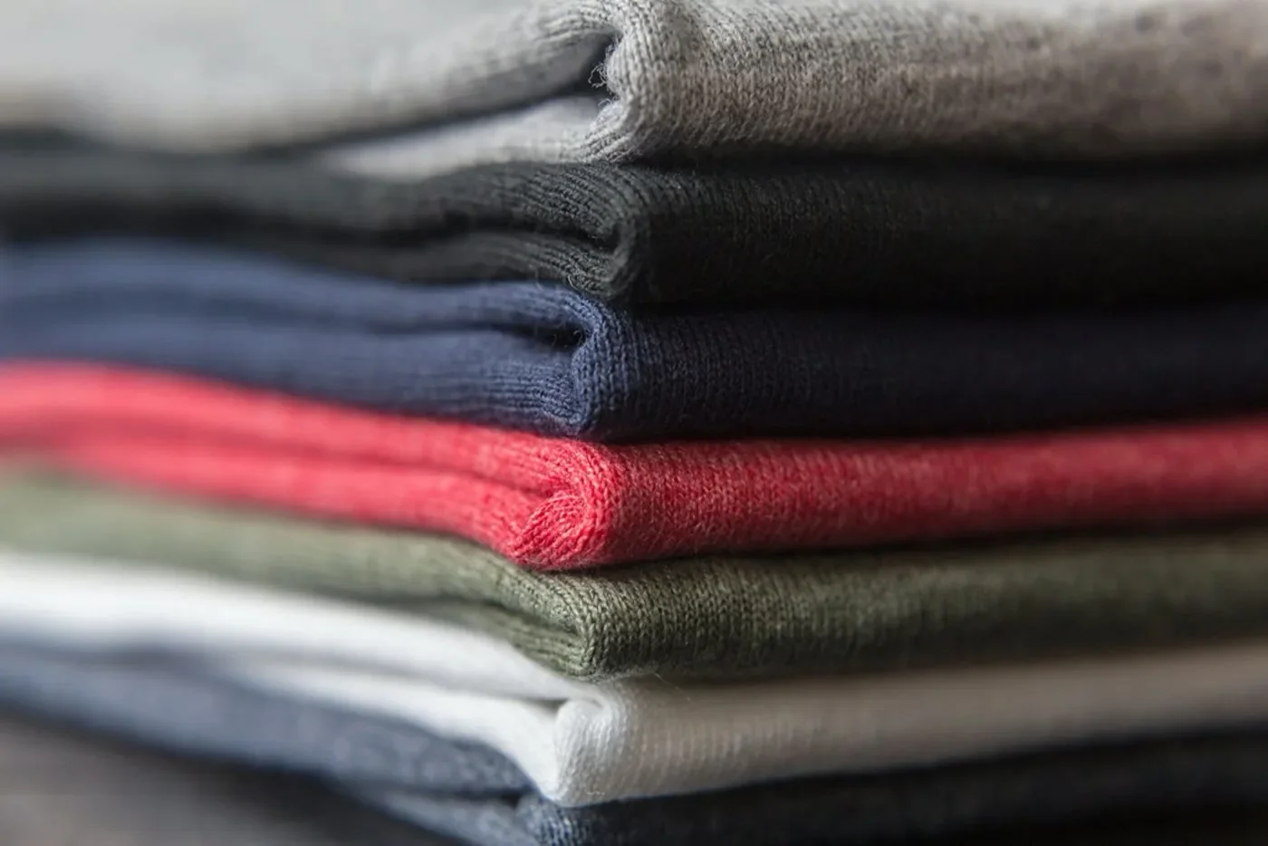 A neatly folded stack of soft cotton shirts in grey, navy, olive, and white